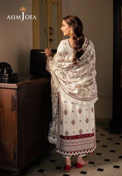 Woman in a traditional embroidered outfit standing in a room with a wooden cabinet.