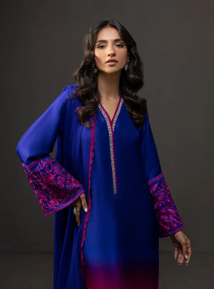 Woman wearing a blue dress with pink embroidery against a dark background