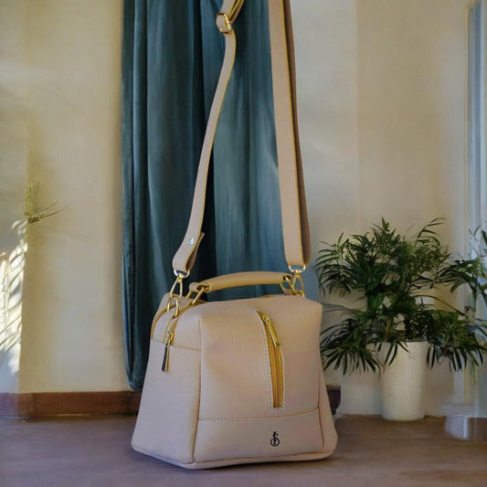Beige handbag with gold accents on a surface with a plant and curtain in the background