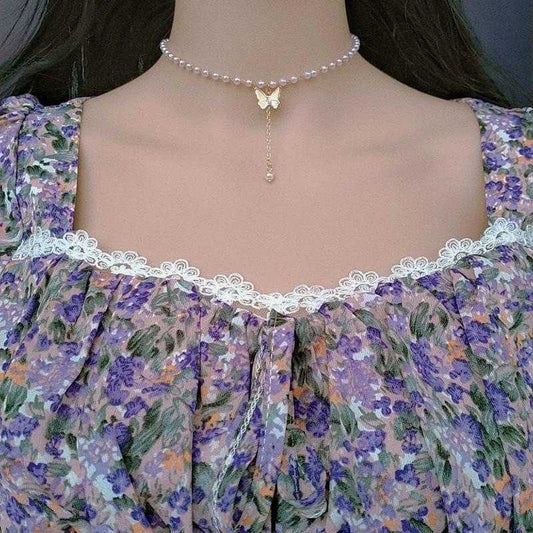 Pearl choker necklace with a butterfly pendant on a floral dress.