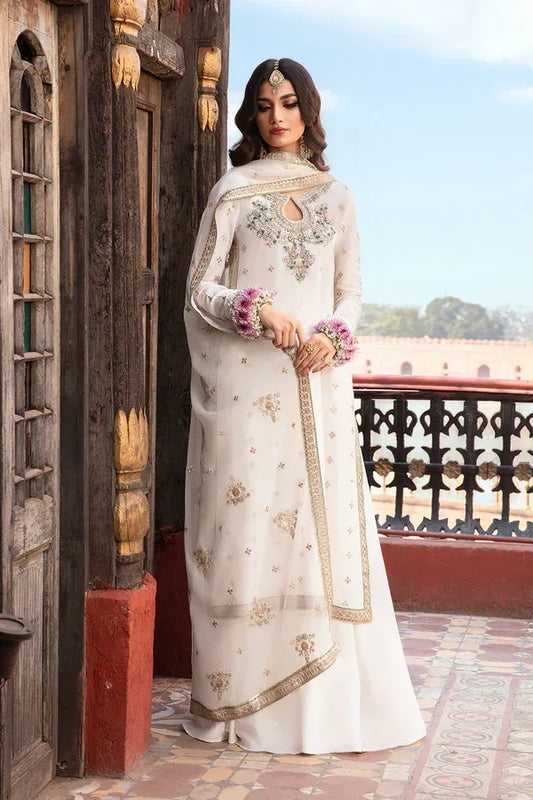 Woman in a white embroidered traditional outfit standing on a balcony with a wooden door and blue sky in the background.