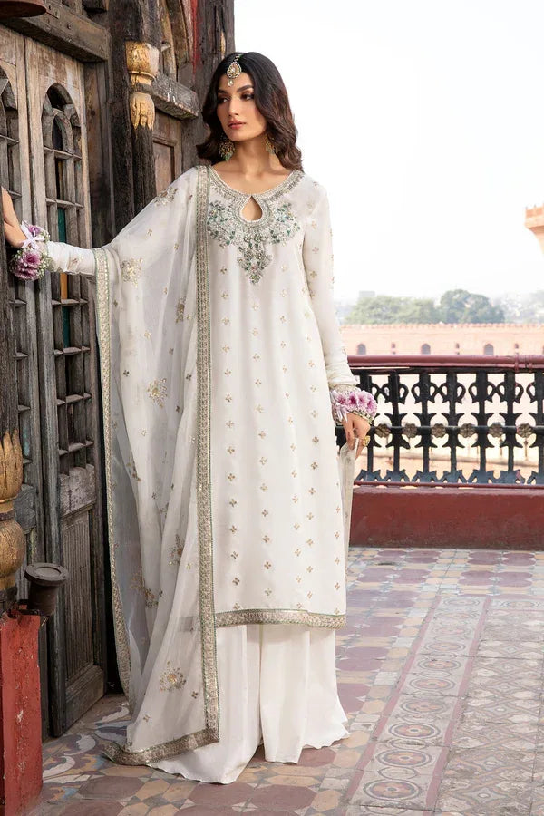 Woman in a white traditional outfit with intricate designs standing in an outdoor setting.