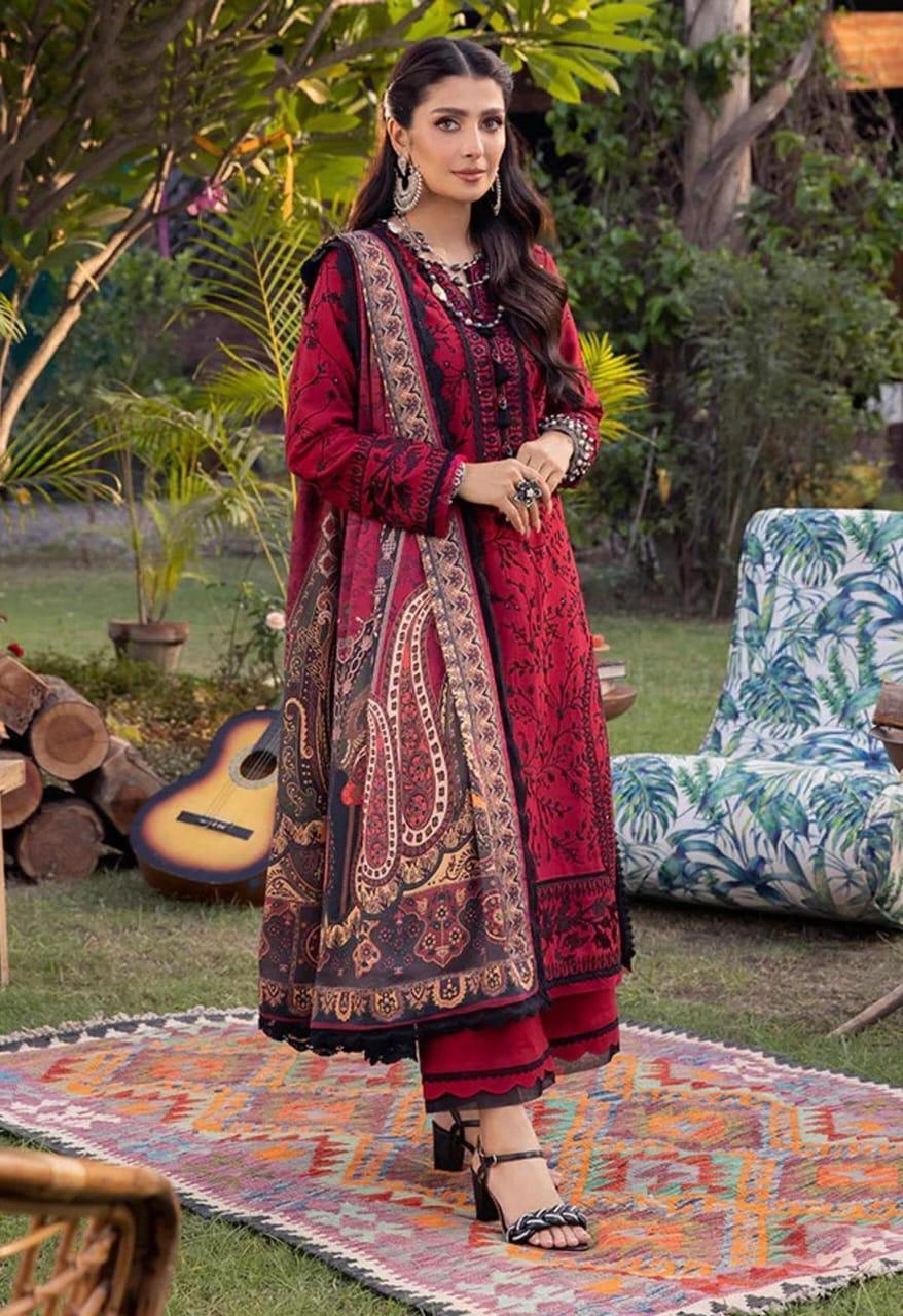 Woman in a red traditional outfit standing outdoors on a colorful rug with plants and furniture in the background.