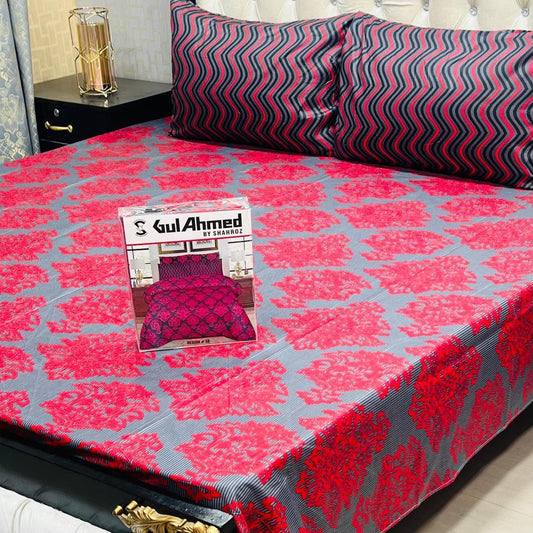 Bedspread with red and gray pattern on a bed, featuring a Gul Ahmed product packaging.