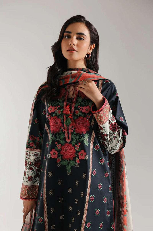 Woman wearing a dark blue embroidered dress with a red and green floral pattern on a plain background