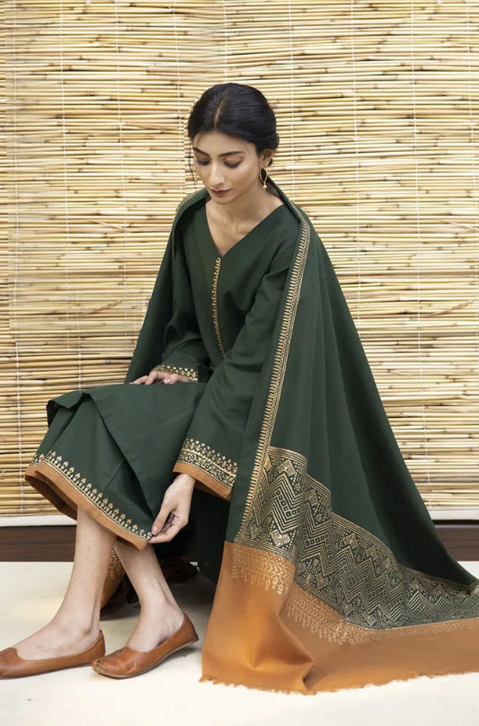 Woman wearing a dark green traditional outfit with gold embroidery against a wooden panel background