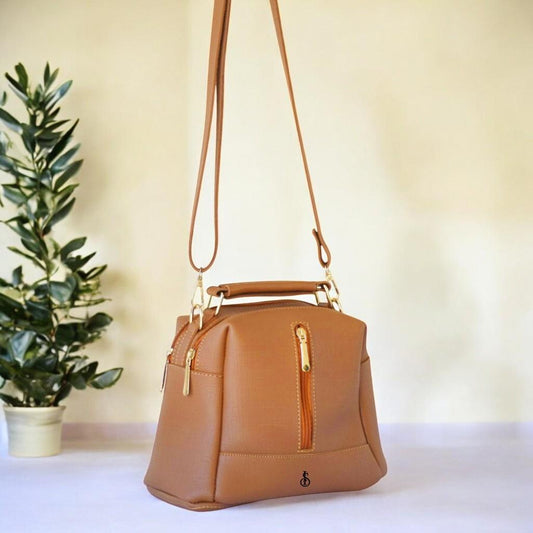 Brown handbag with gold accents on a white surface with a plant in the background