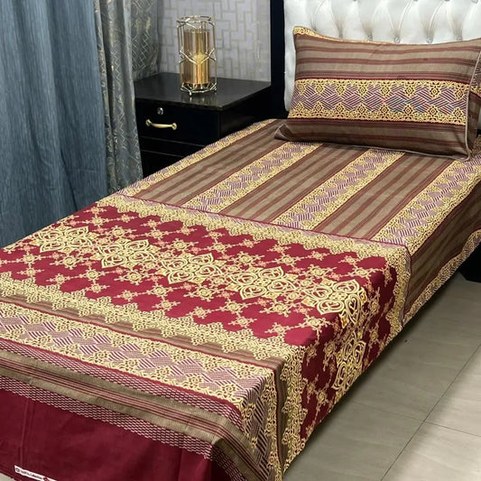 Decorative bedspread with red and gold patterns on a bed in a bedroom setting.
