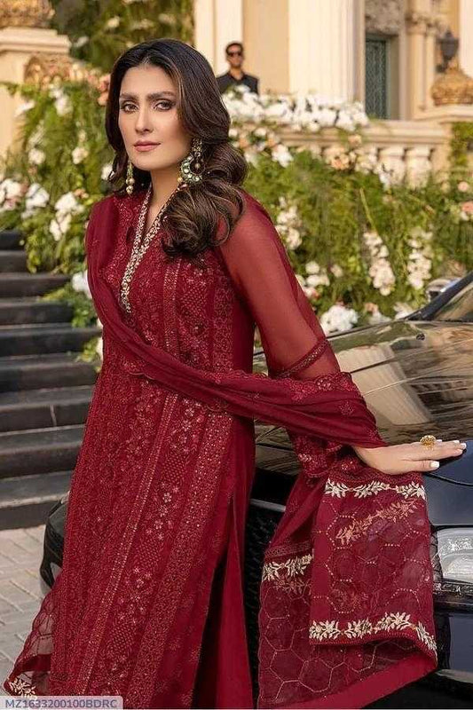 Woman in a red traditional outfit standing in front of a decorated outdoor setting with flowers and architecture.