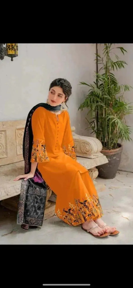 Woman in an orange and black traditional outfit sitting on a couch with a plant in the background