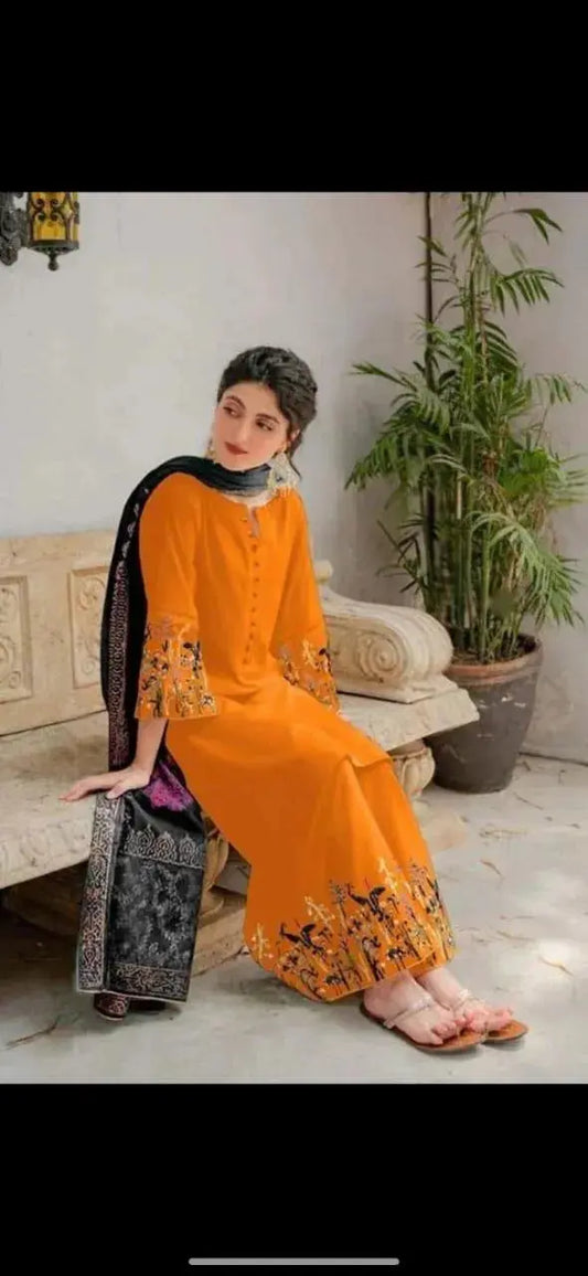 Woman in an orange and black traditional outfit sitting on a couch with a plant in the background