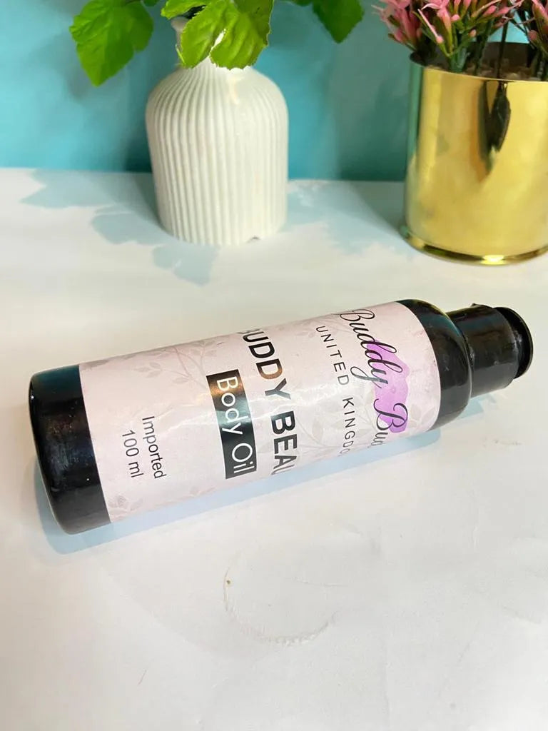 Buddy Beauty body oil bottle on a white surface with decorative vases in the background.