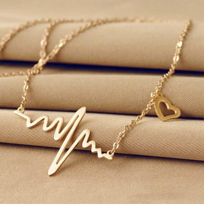 Gold necklace with a heart and wave design on a beige surface