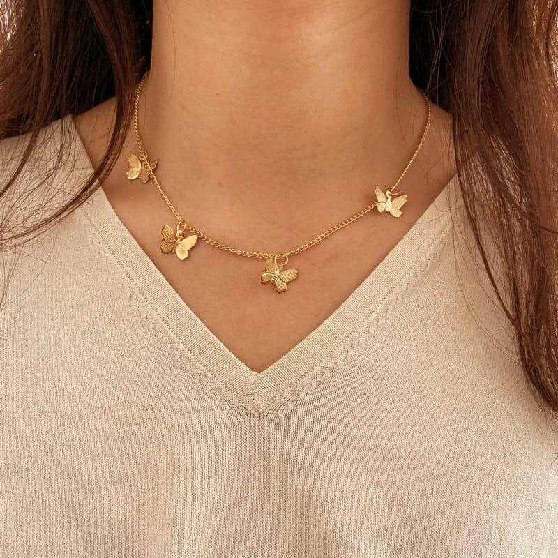 Gold butterfly necklace worn by a person on a beige background