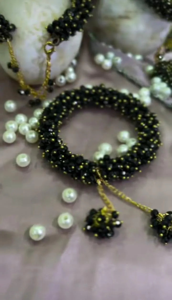 Black beaded bracelet with gold accents and pearls on a neutral background