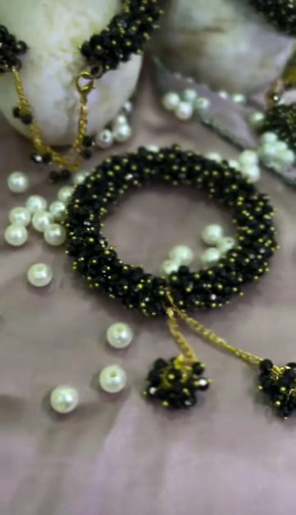 Black beaded bracelet with gold accents and pearls on a neutral background
