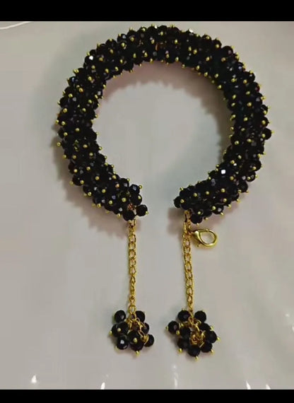Black beaded bracelet with gold chain and flower-shaped ends on a white background