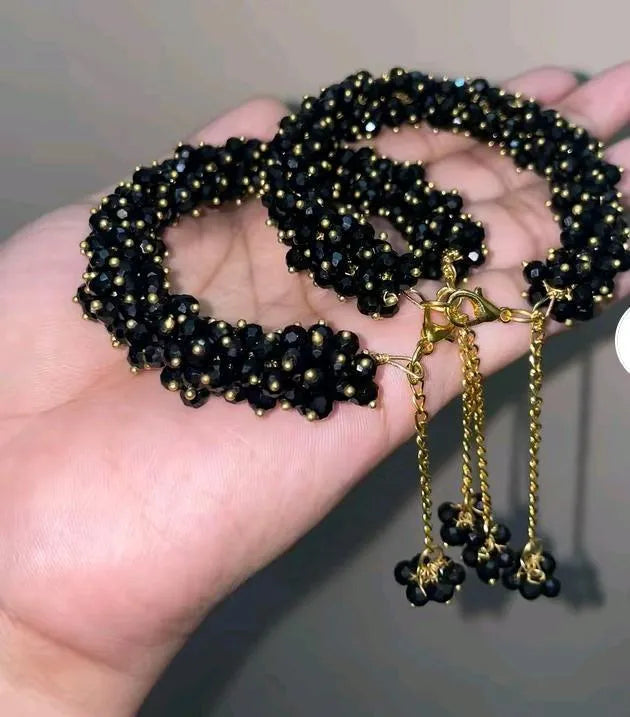 Black beaded necklace with gold chain held in a hand against a neutral background