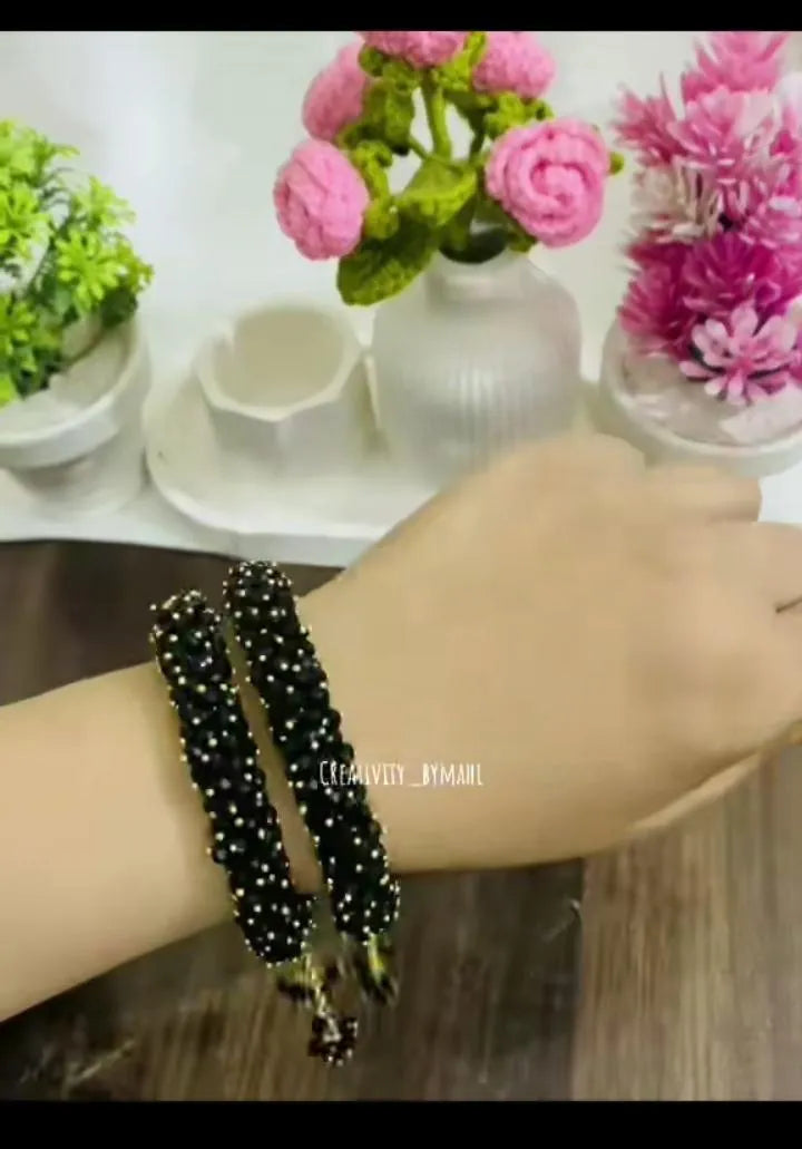 Black beaded bracelet on a wrist with a blurred background of flowers and decor.