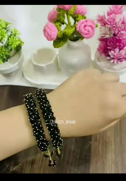Black beaded bracelet on a wrist with a blurred background of flowers and decor.