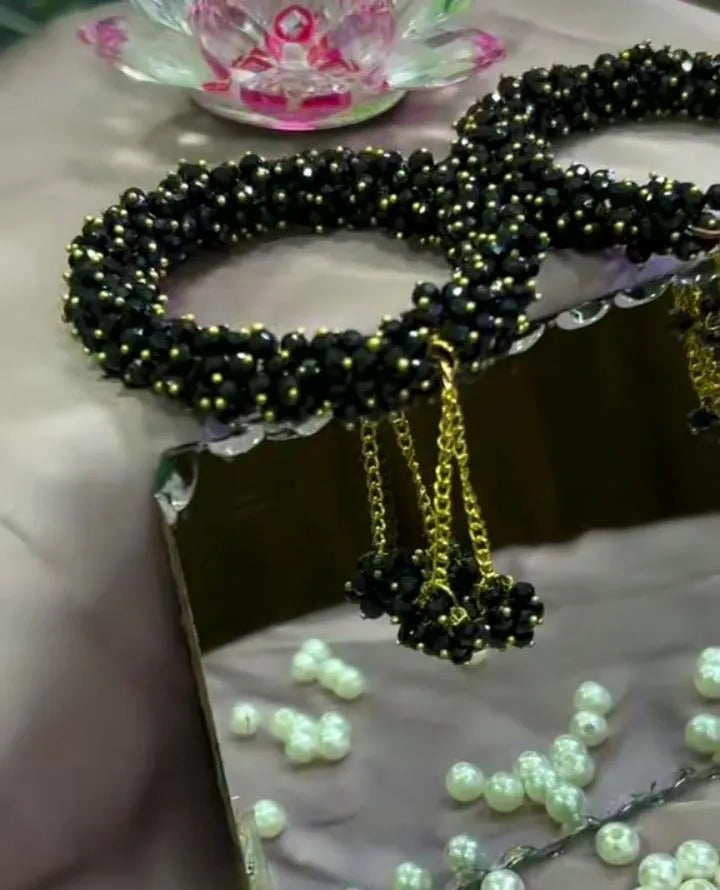 Black beaded necklace with gold chain on a reflective surface