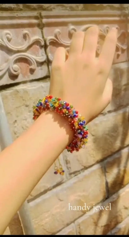 Hand wearing a colorful beaded bracelet against a decorative stone wall, with 'handy jewel' branding.