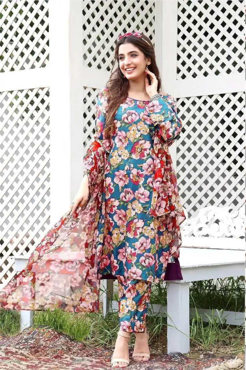 Woman wearing a floral dress and pants set standing in front of a white lattice fence.