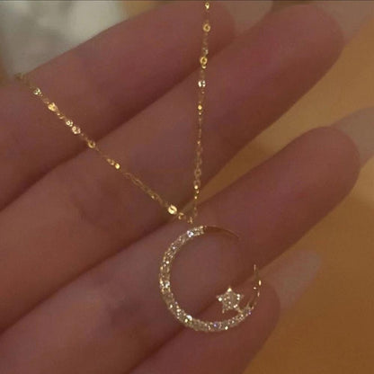 Gold necklace with a crescent moon and star pendant held in a hand against a blurred background