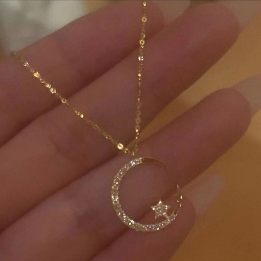 Gold necklace with a crescent moon and star pendant held in a hand against a blurred background