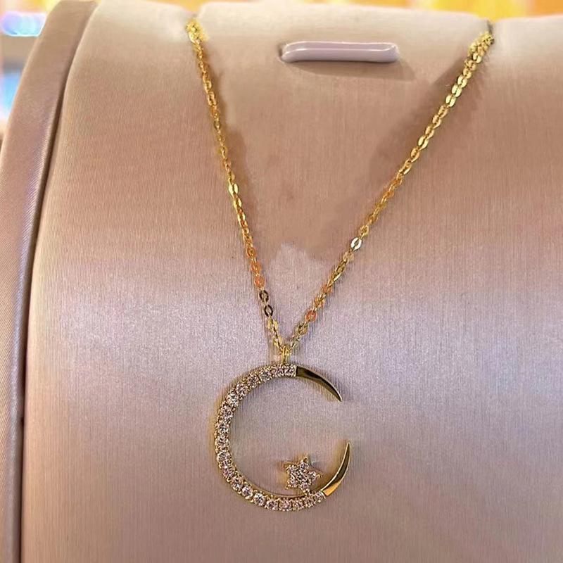 Gold necklace with a crescent moon and star pendant on a pink cushion