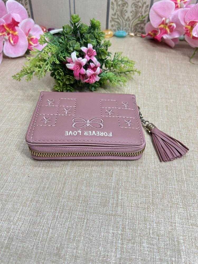 Pink wallet with tassel on a textured surface with flowers in the background