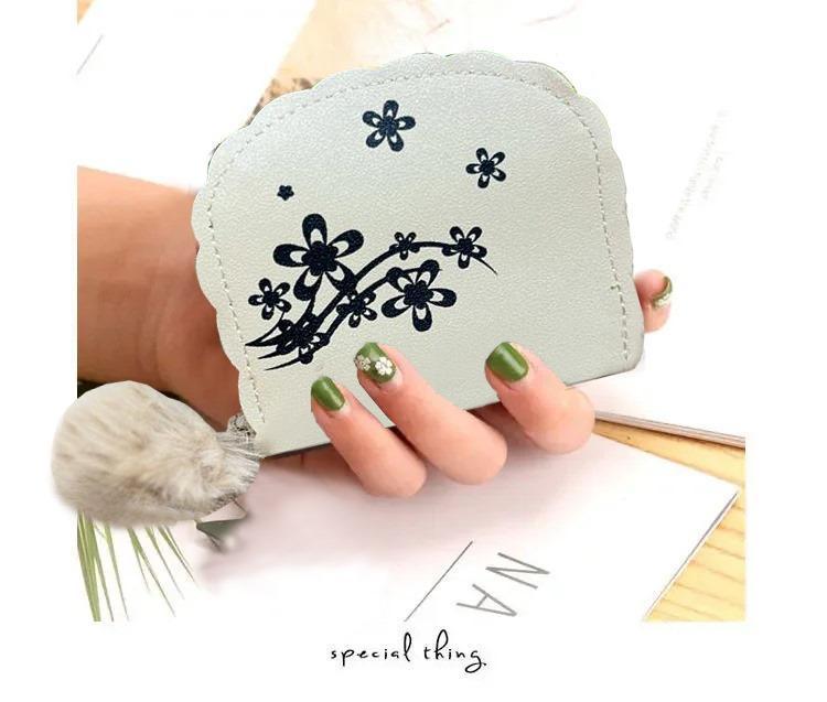 Light blue wallet with floral design held by a hand with green nail polish.