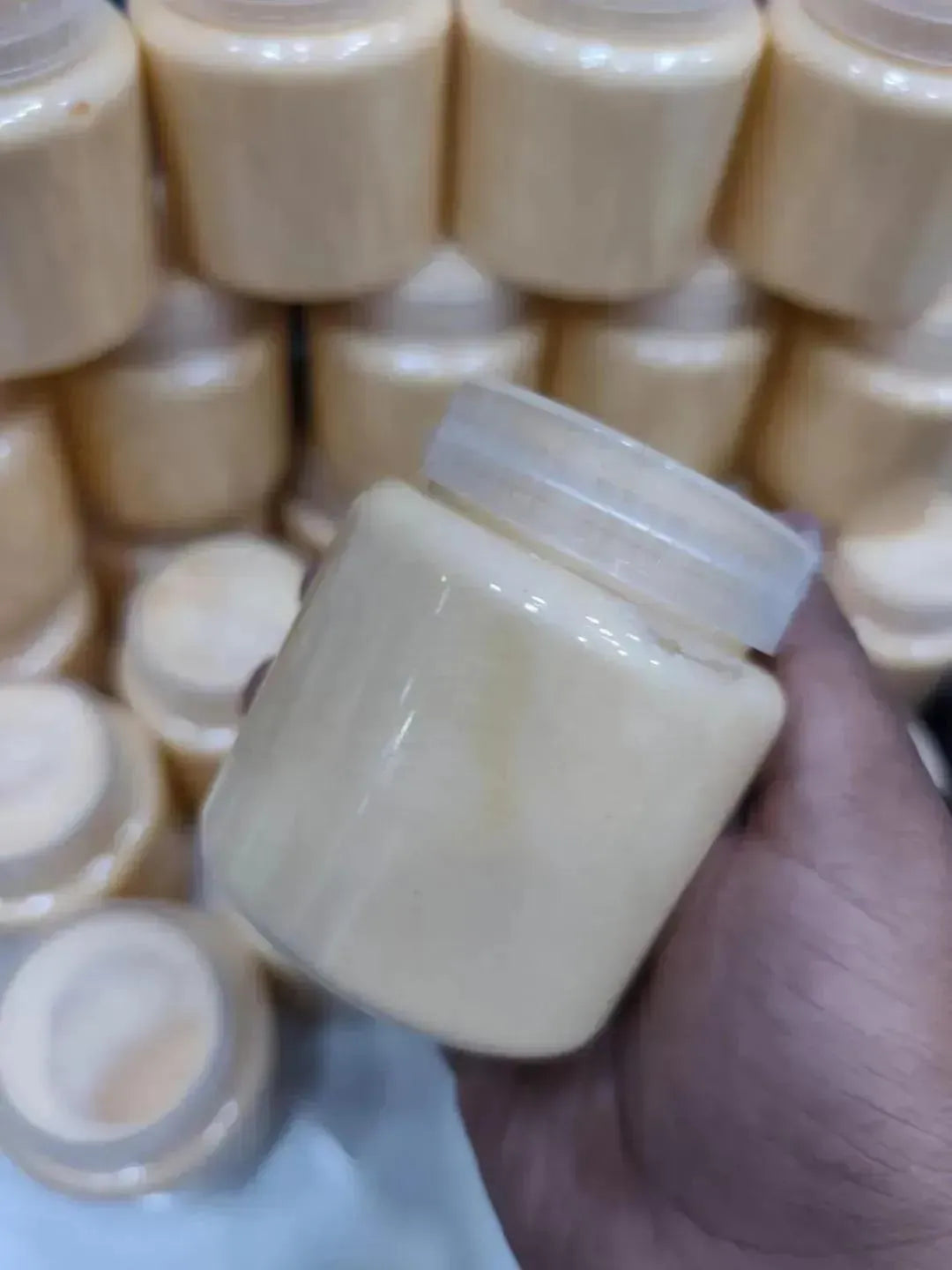 Hand holding a small jar of cream with stacked jars in the background