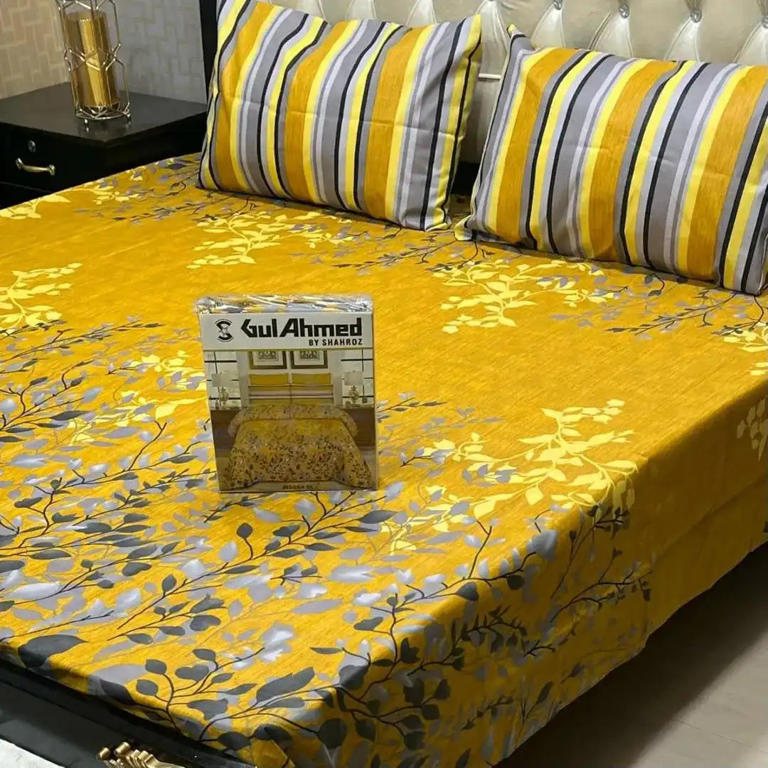Yellow and gray floral patterned bedspread on a bed with striped pillows, featuring Gul Ahmed branding.