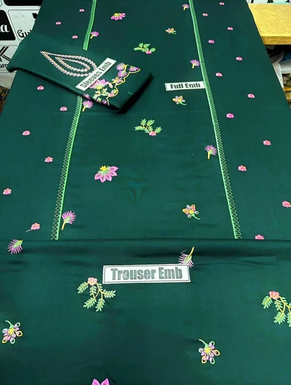 Green fabric with floral embroidery and 'Trouser Emb' label on a table.