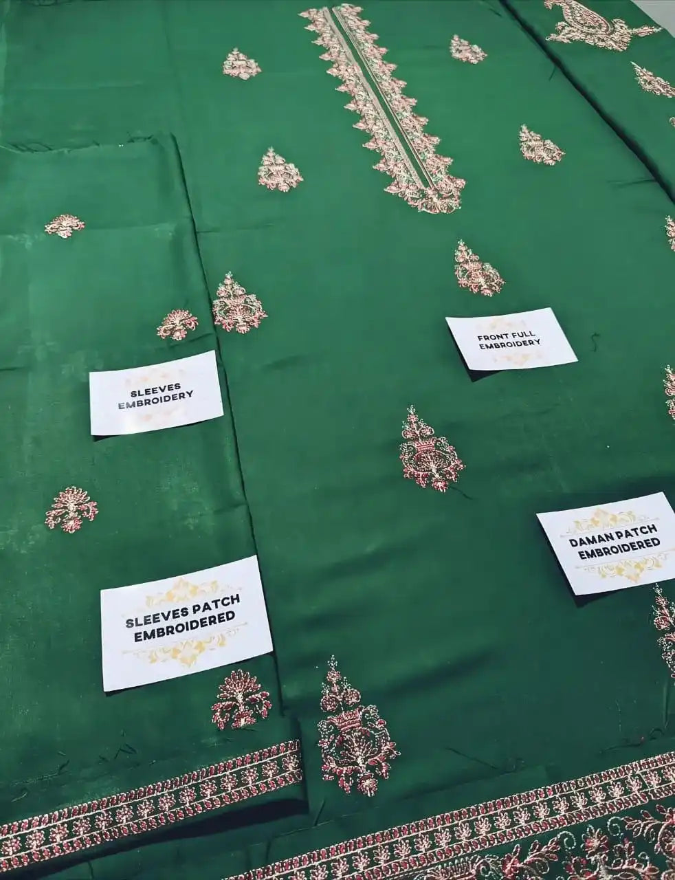 Green fabric with embroidered patterns and labels indicating embroidery details.