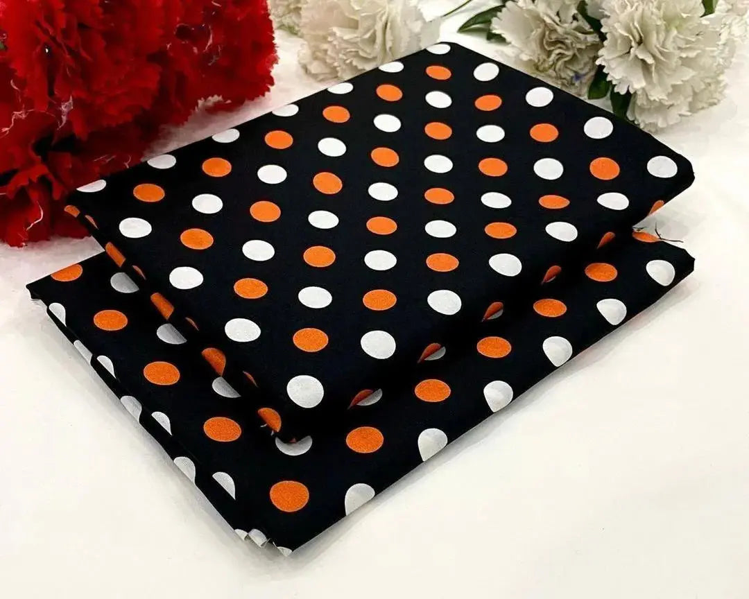 Black fabric with orange and white polka dots on a white surface with flowers in the background