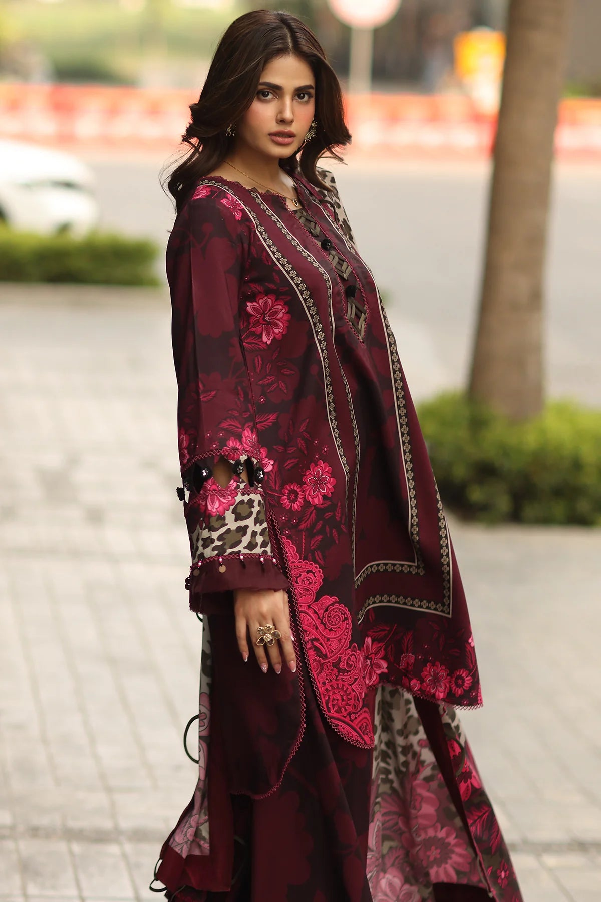 Woman wearing a maroon embroidered traditional outfit with a blurred outdoor background