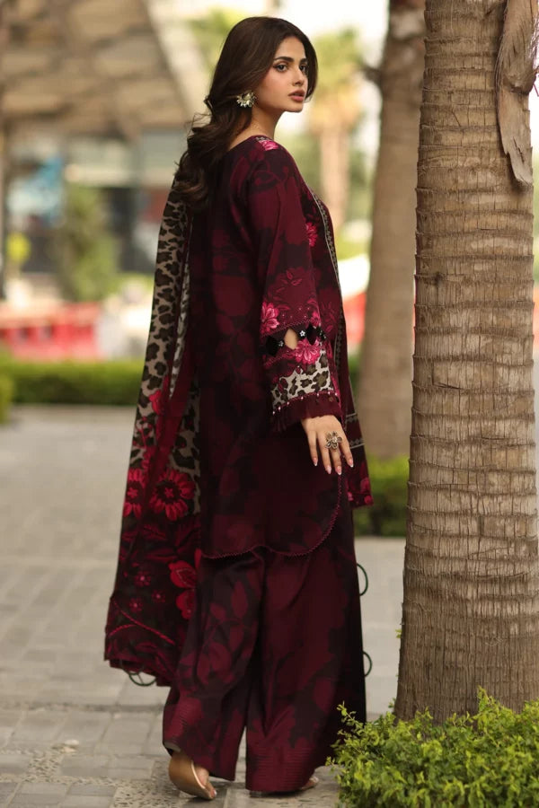 Woman in a maroon traditional outfit with floral patterns standing next to a palm tree.