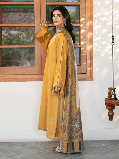 Woman in a yellow traditional outfit with intricate patterns standing indoors.