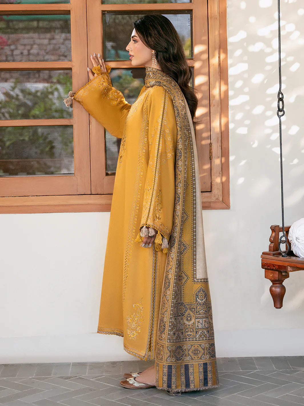 Woman in a mustard yellow traditional outfit with intricate patterns standing indoors.
